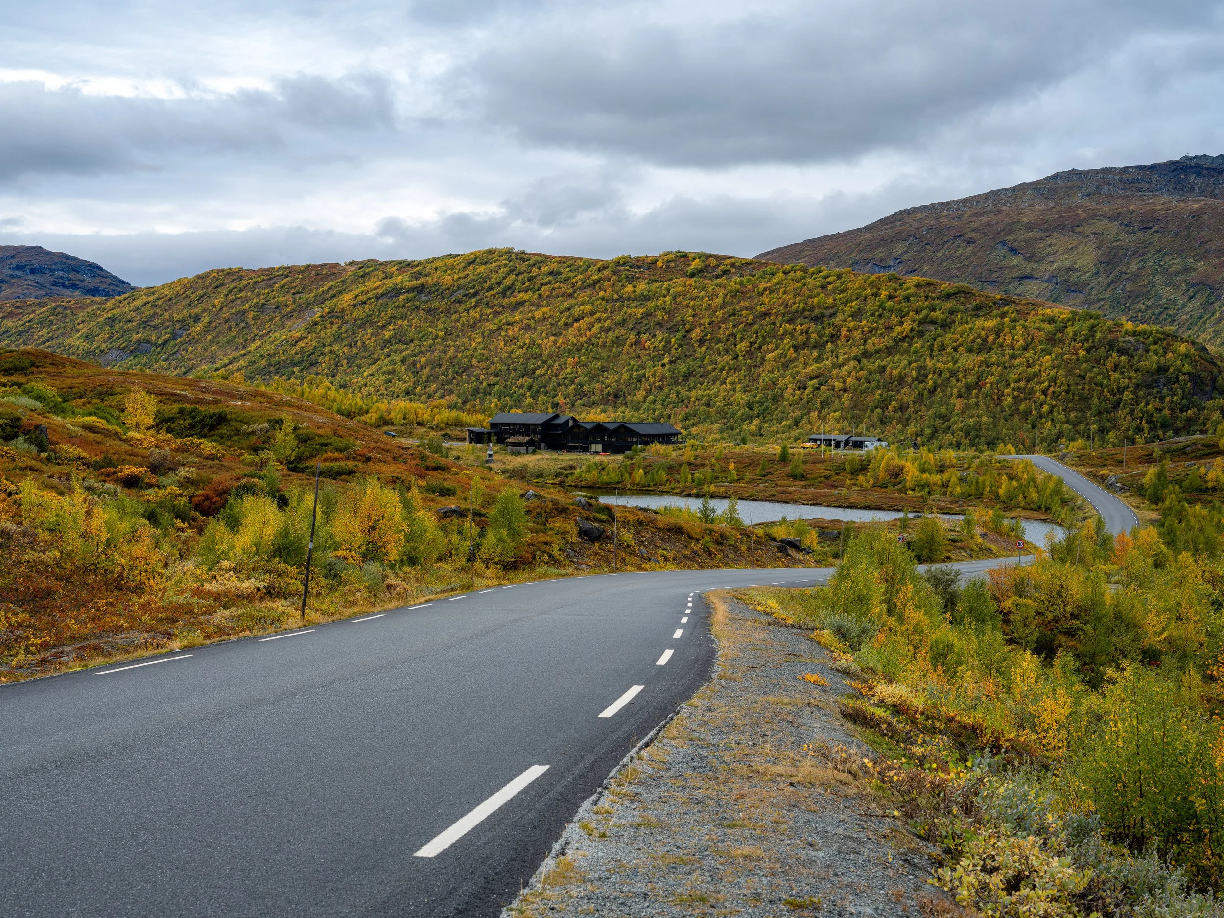 En svingete vei gjennom fjell og høstfarger i Norge. Jotunheimen Fjellstue i bakgrunnen. 