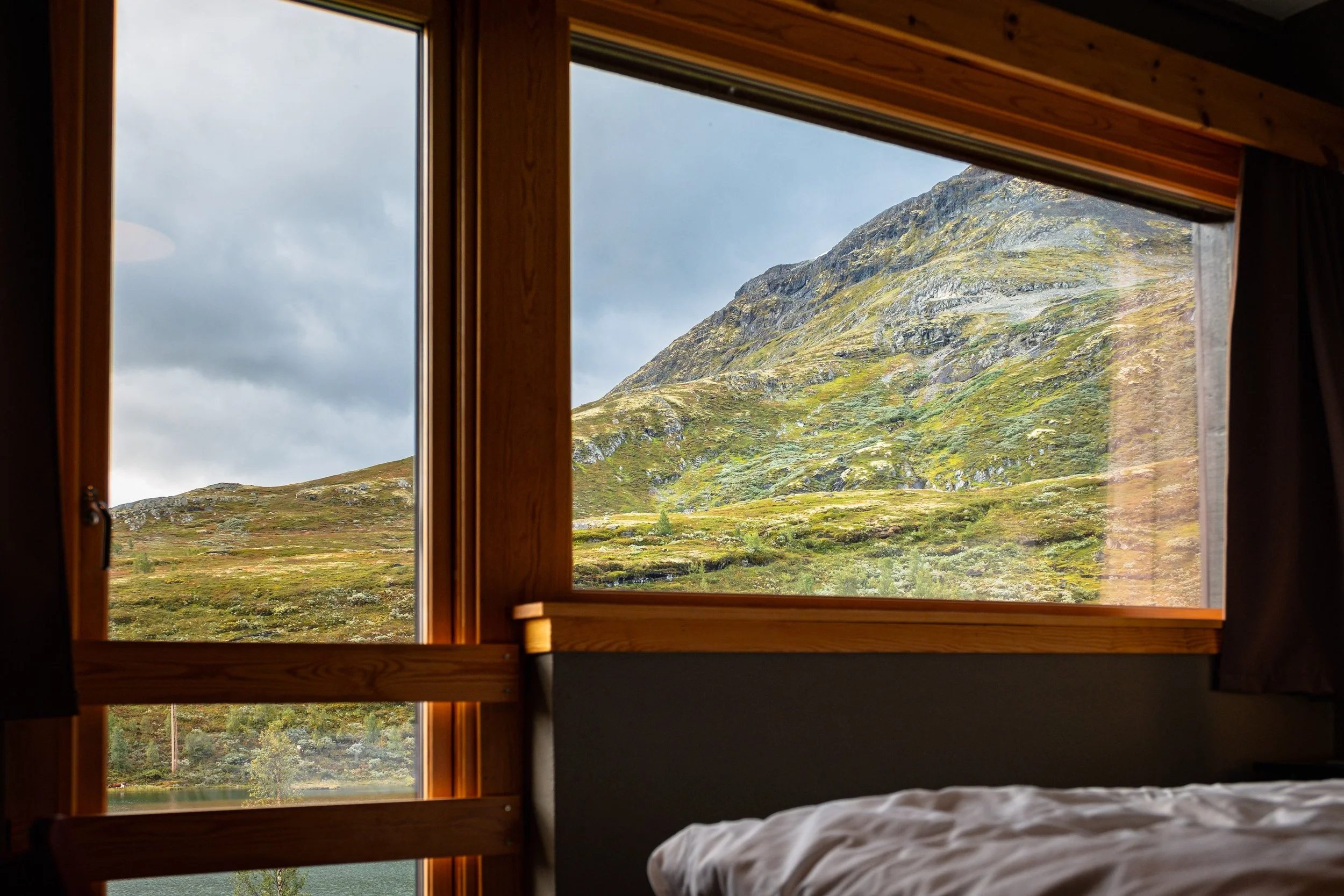 Utsikt fra soverom med store vinduer ut mot fjelllandskap med grønne og steinete fjell.