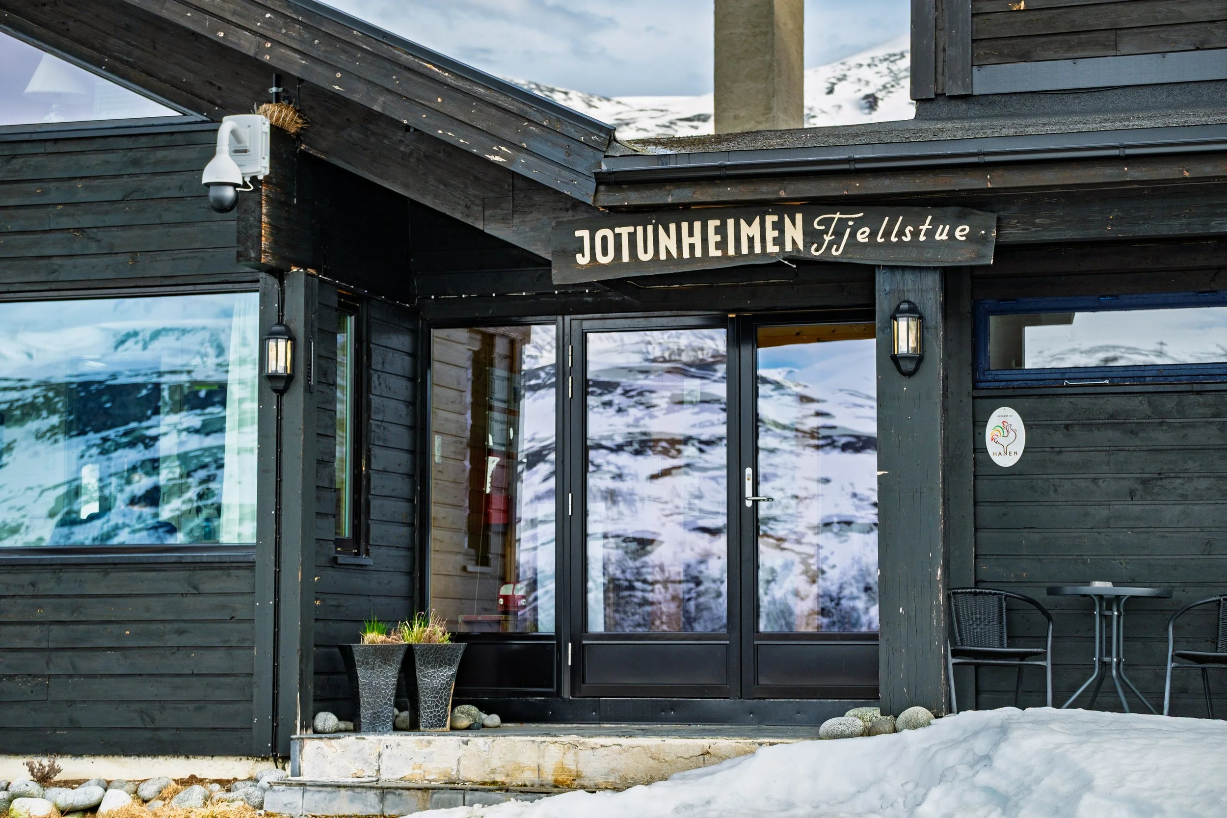 Inngangsdør til Jotunheimen Fjellstue, snødekke foran inngangen, fjell og vinterlandskap i bakgrunnen.