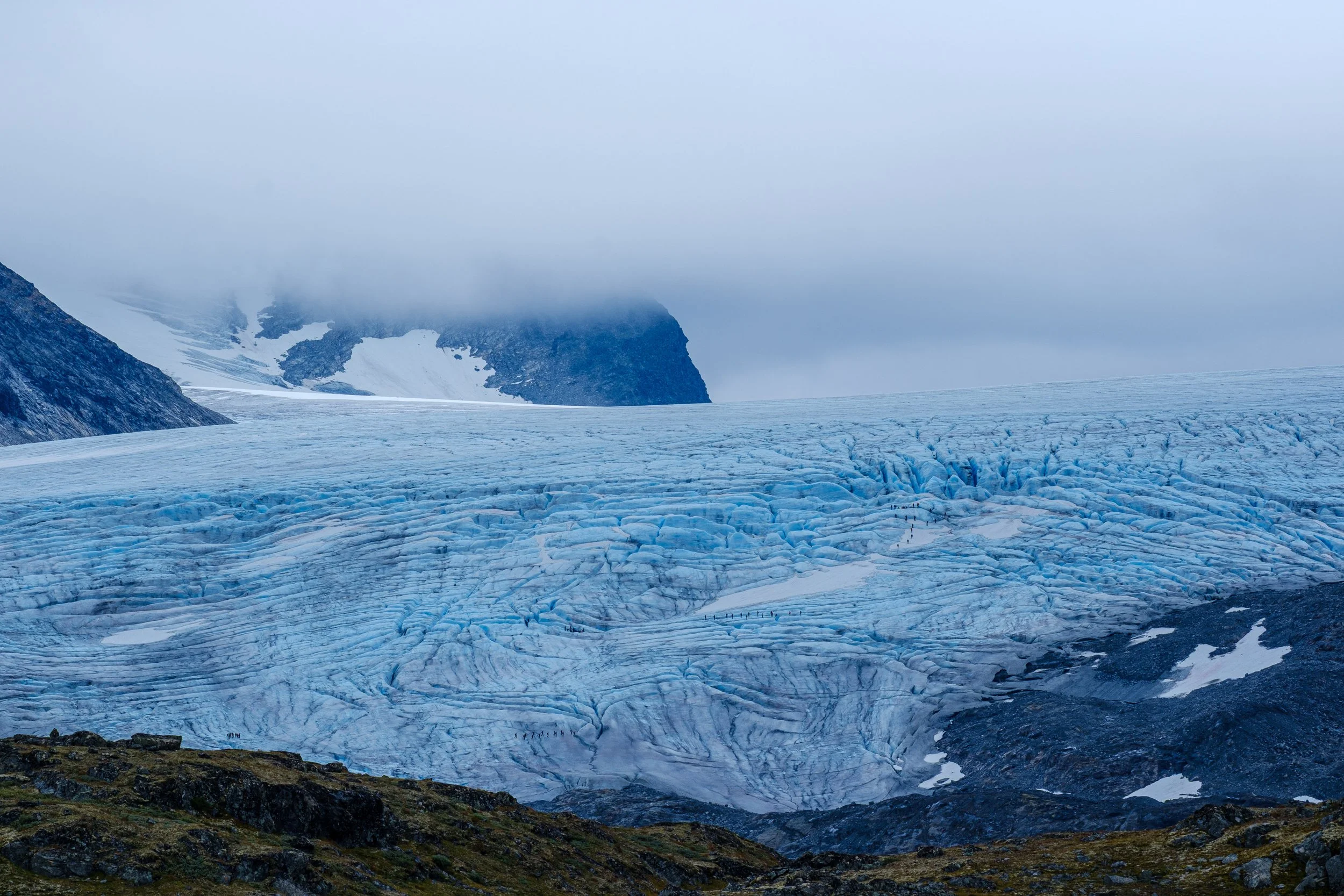 En stor isbre med sprekker, omgitt av fjell og tåkete vær.