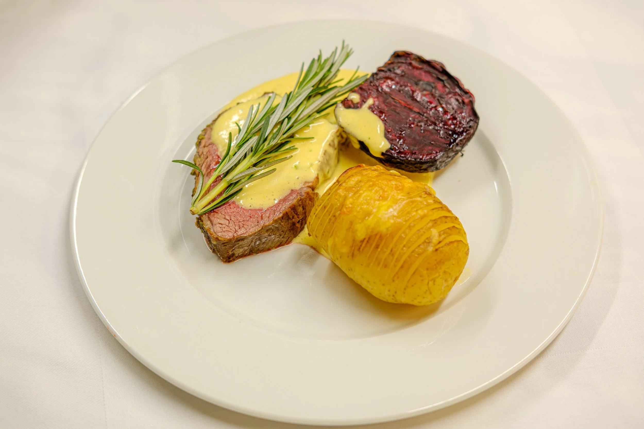 Tallerken med biffstykke med stekte grønne urter, saus og potet.