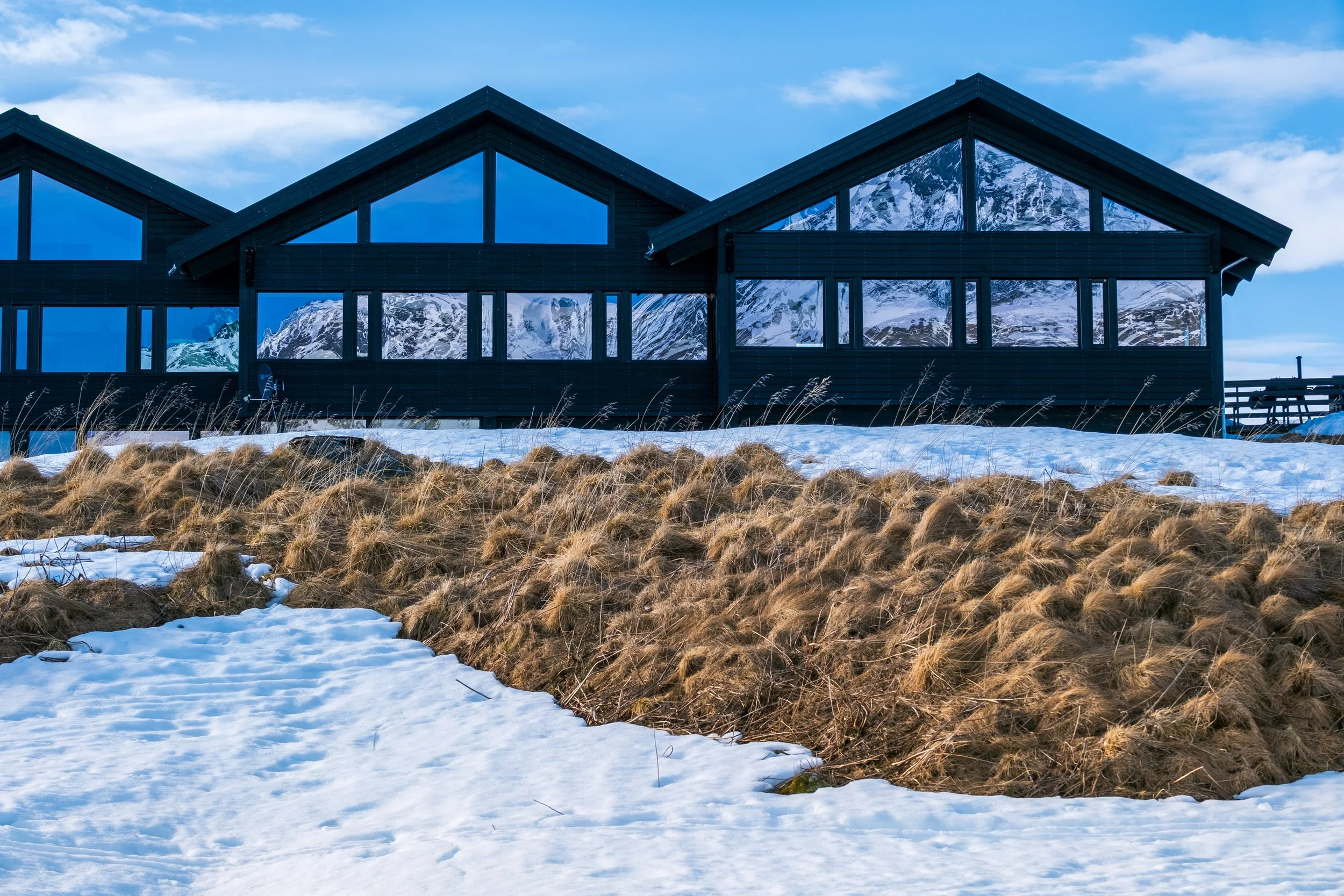 Deler av Jotunheimen Fjellstue med store glassvinduer og snødekt utendørsområde, omgitt av fjelllandskap.