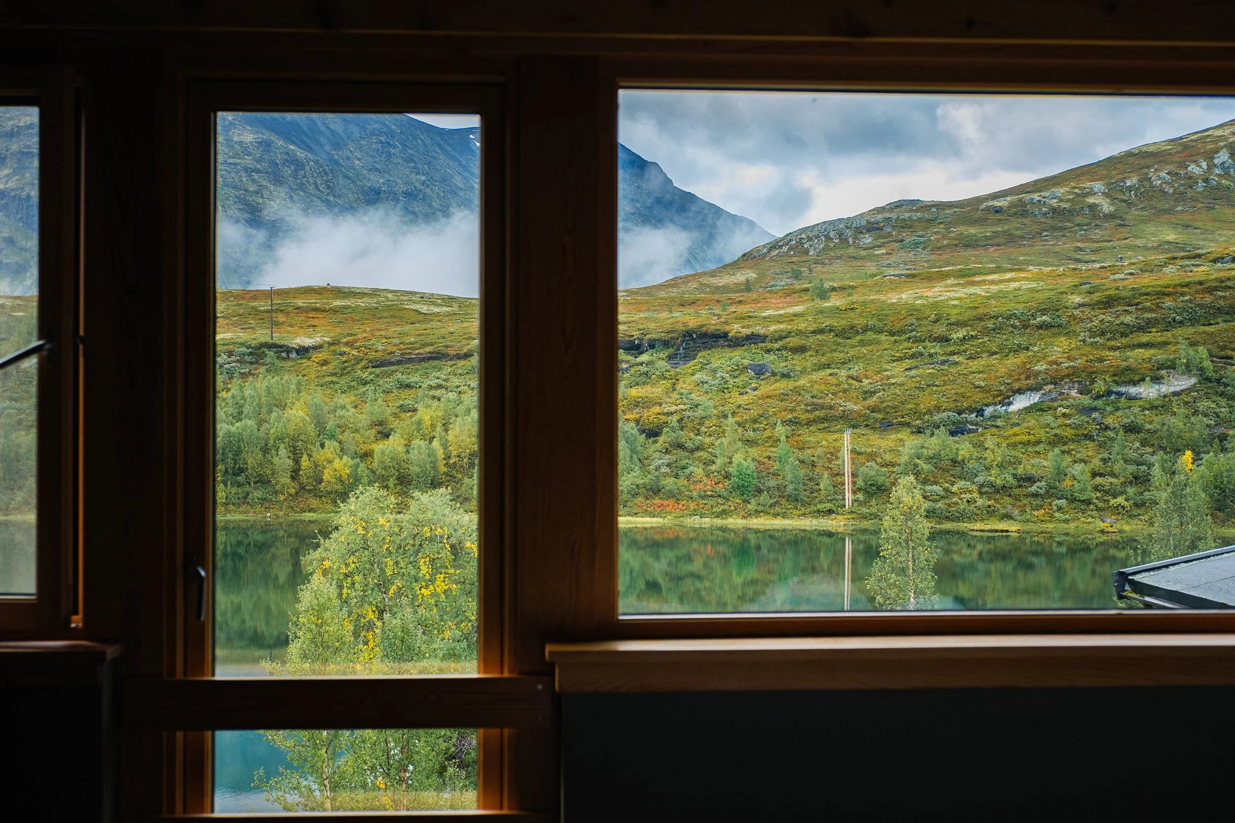 Utsikt gjennom et trevindu med fjell, sjø og skog i bakgrunnen.