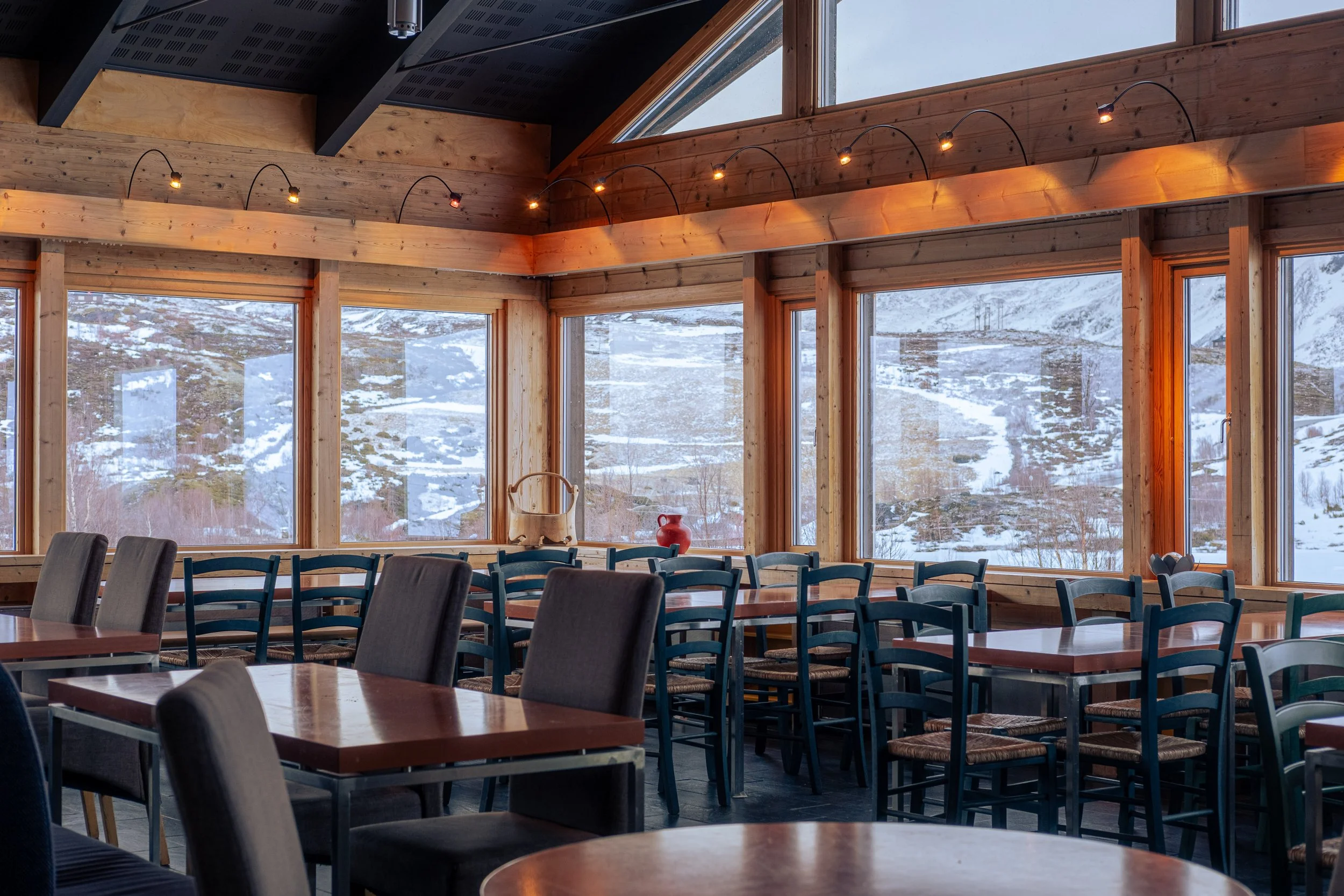 Frokost og kafesalen med store vinduer som viser snødekt fjellandskap, flerfargede stoler og trevegger.