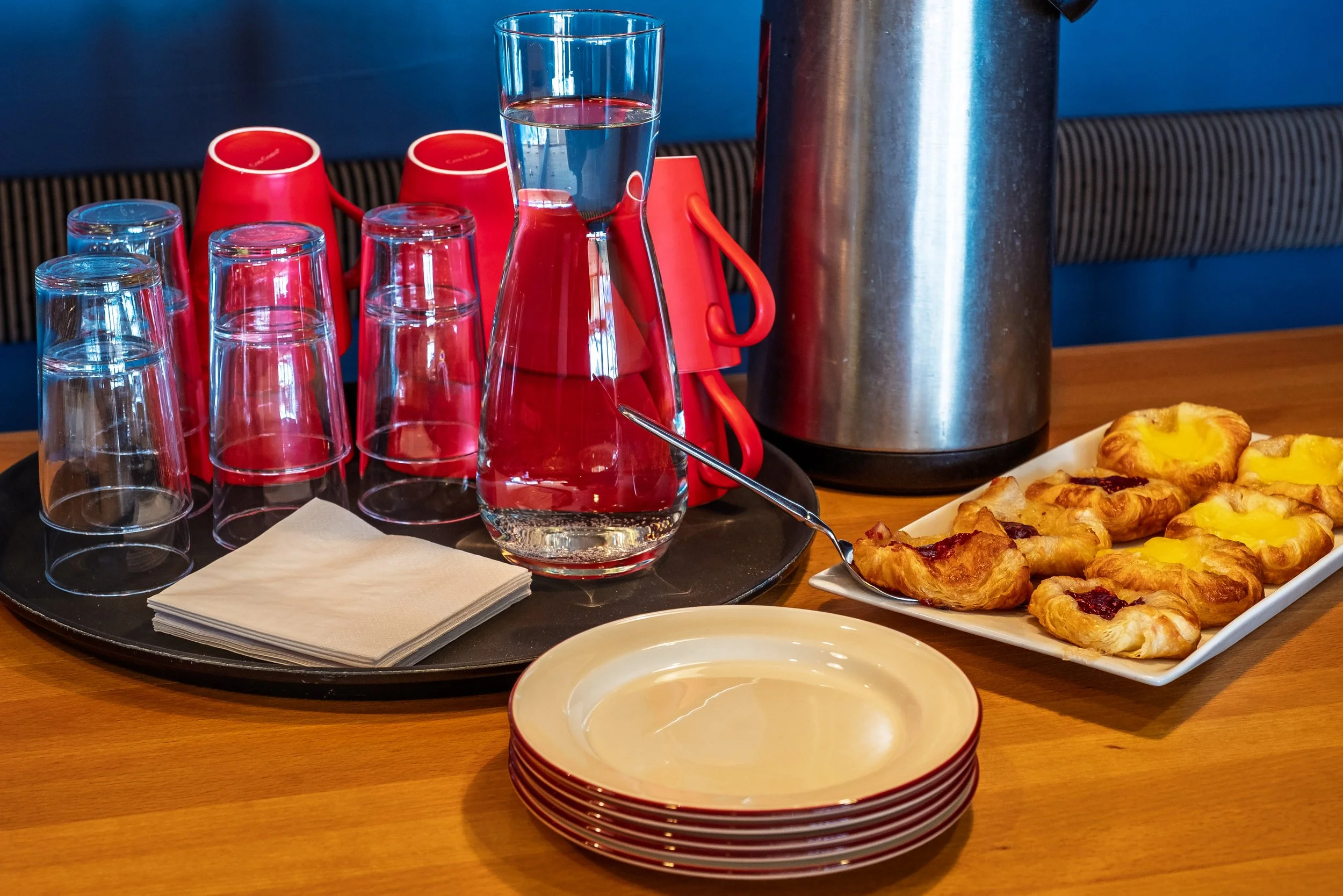 Et serveringsbrett med tomme glass og en kaffekanne, pluss en tallerken med små bakverk med frukt eller syltetøy i, på et trebord.