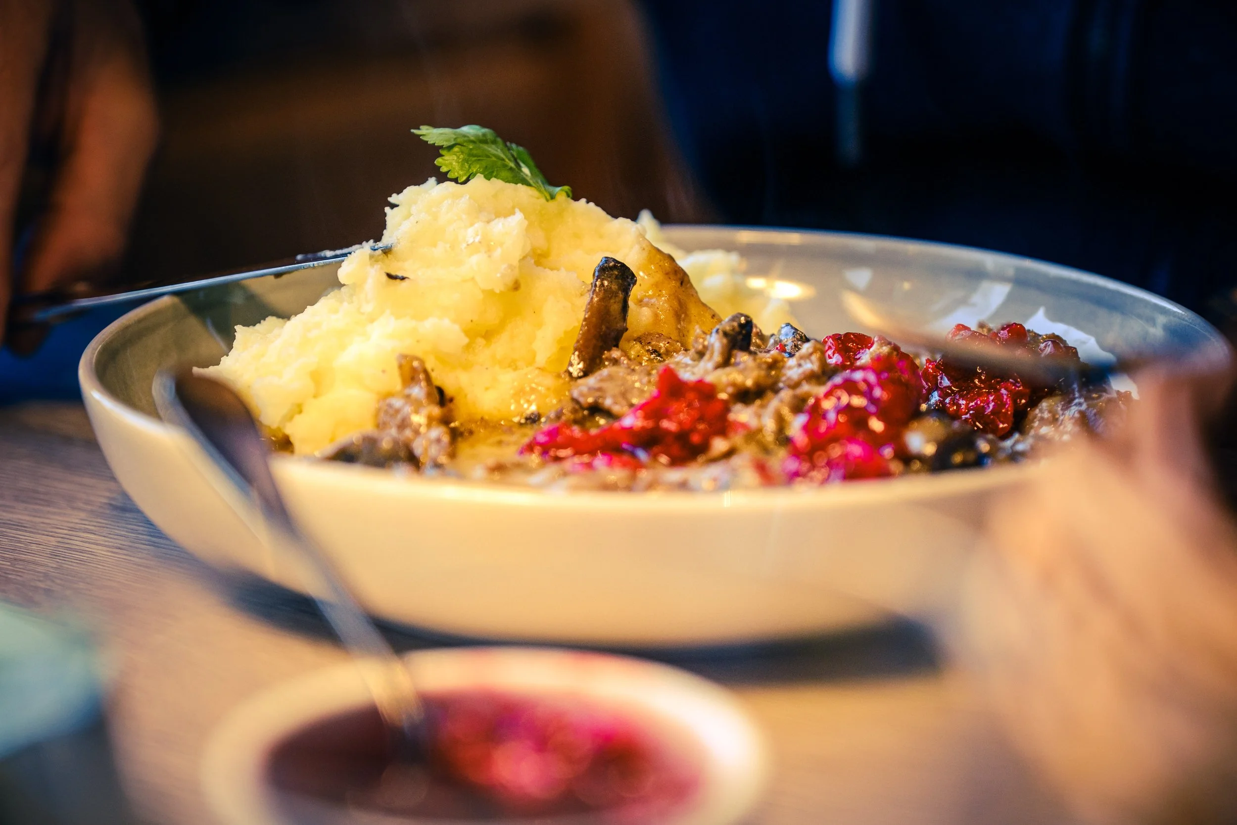 Bilde av en bolle med potetmos og kjøttgryte medtyttebær, pyntet med en frisk urter på toppen.