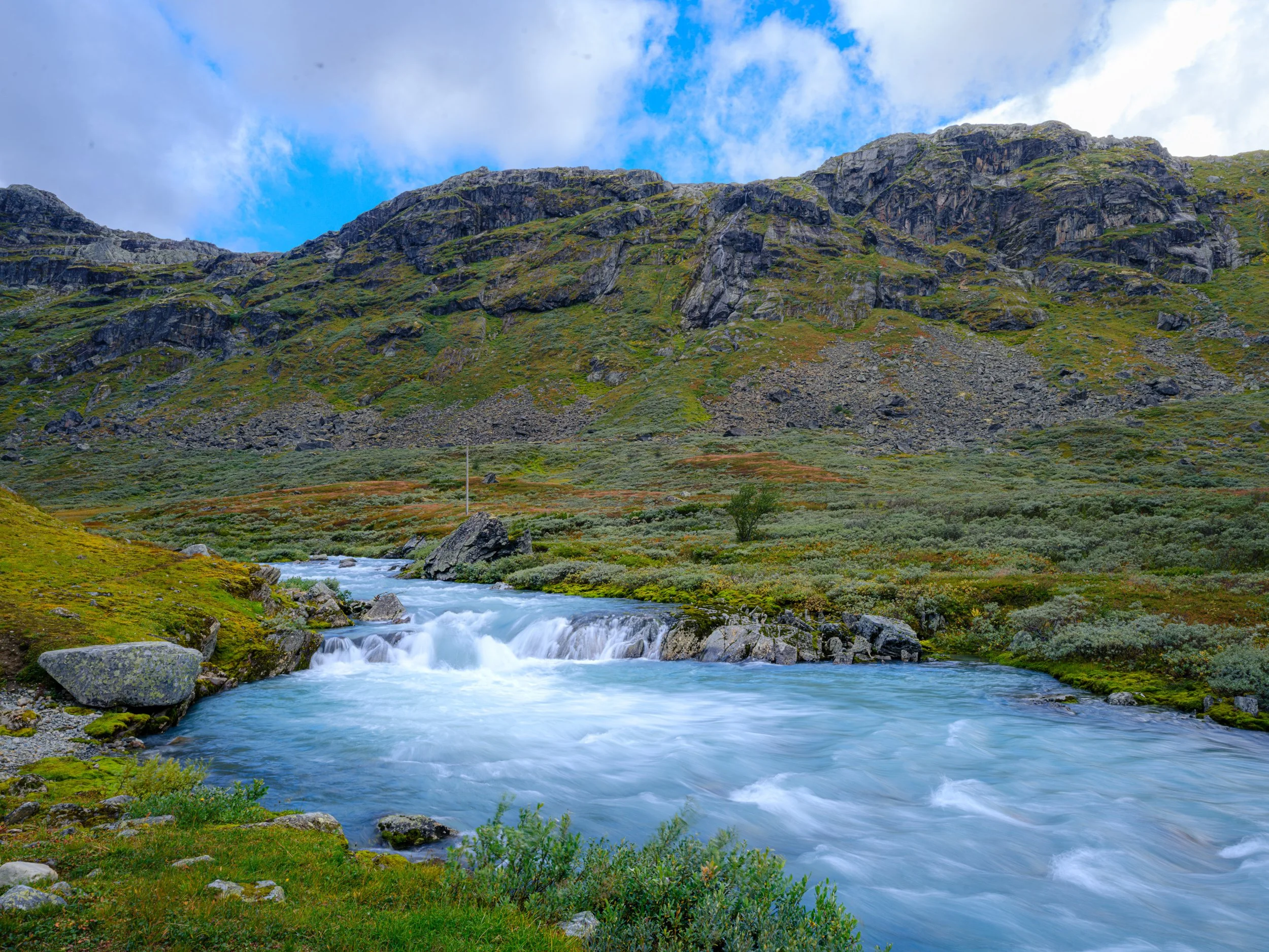 Elv som renner gjennom grønn dal omgitt av fjell.
