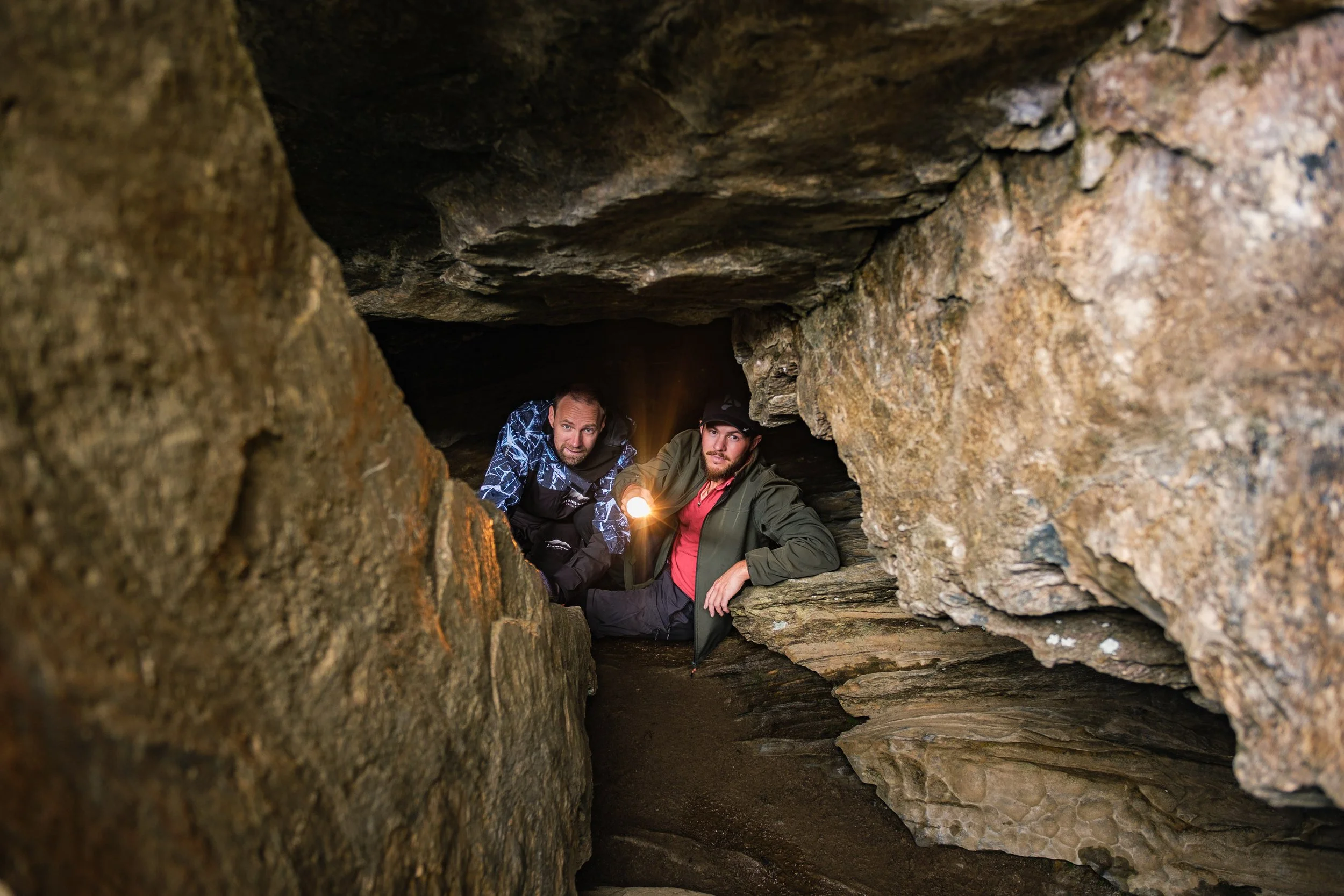 To menn på grottevandring inne i grotten, den ene holder en lommelykt.