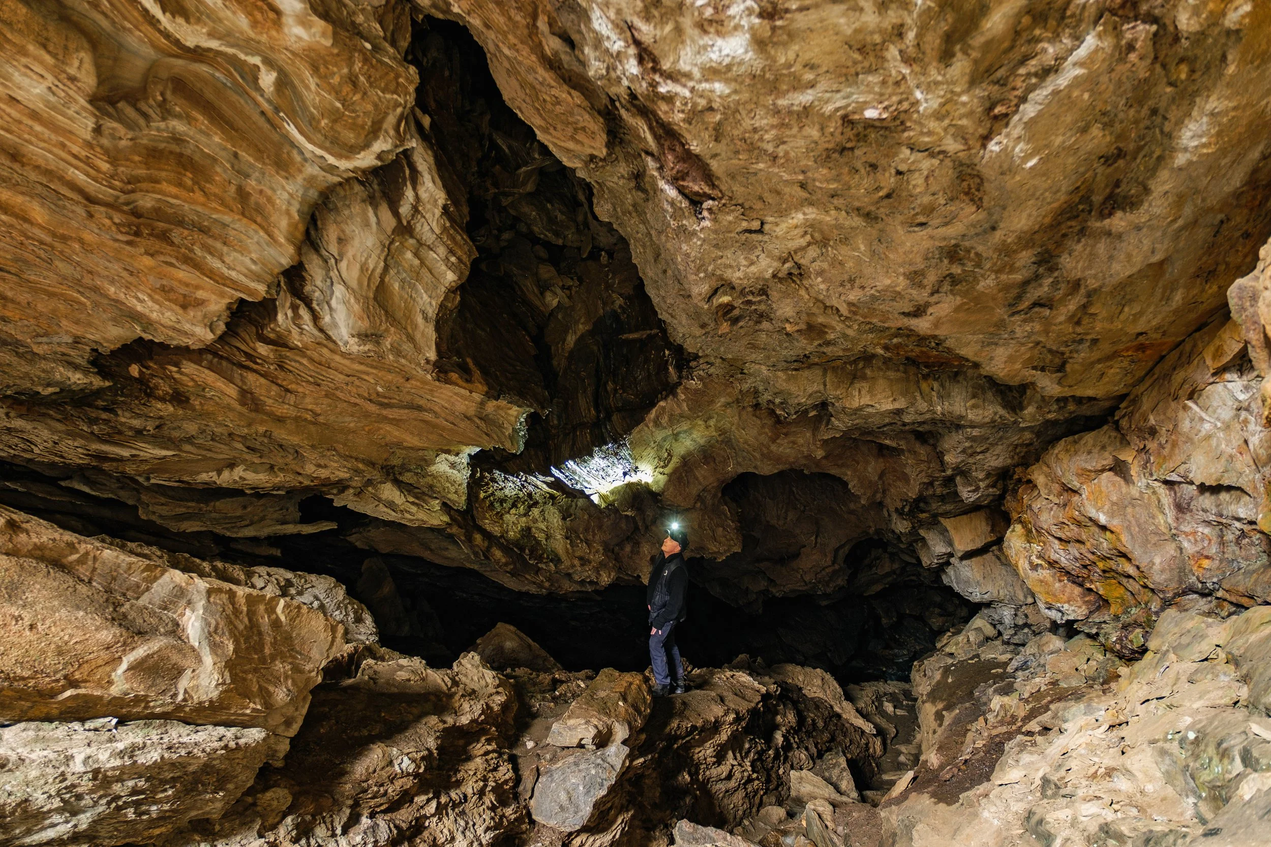 En person med hodelykt står inne i en stor grotte med tak og vegger av faste stein. 