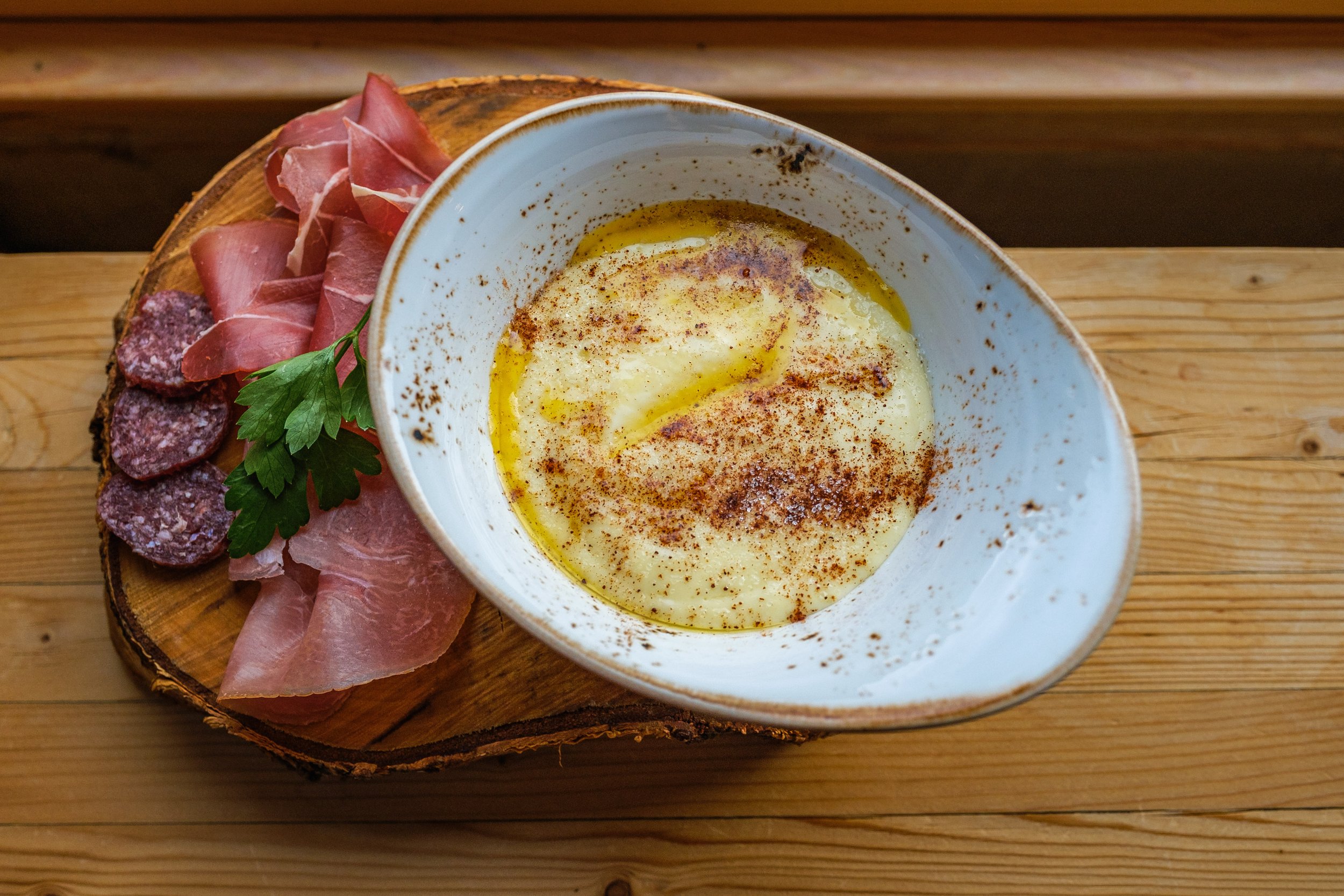 En middagskål med rømmegrøt, plassert på en treplate sammen med spekeskinke på en trebord.