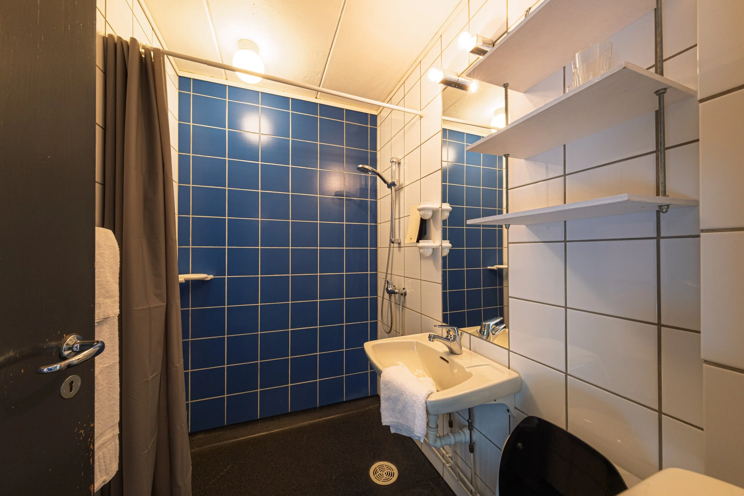 Private bad med speil, vask, dusj, toalett og hyller for oppbevaring.