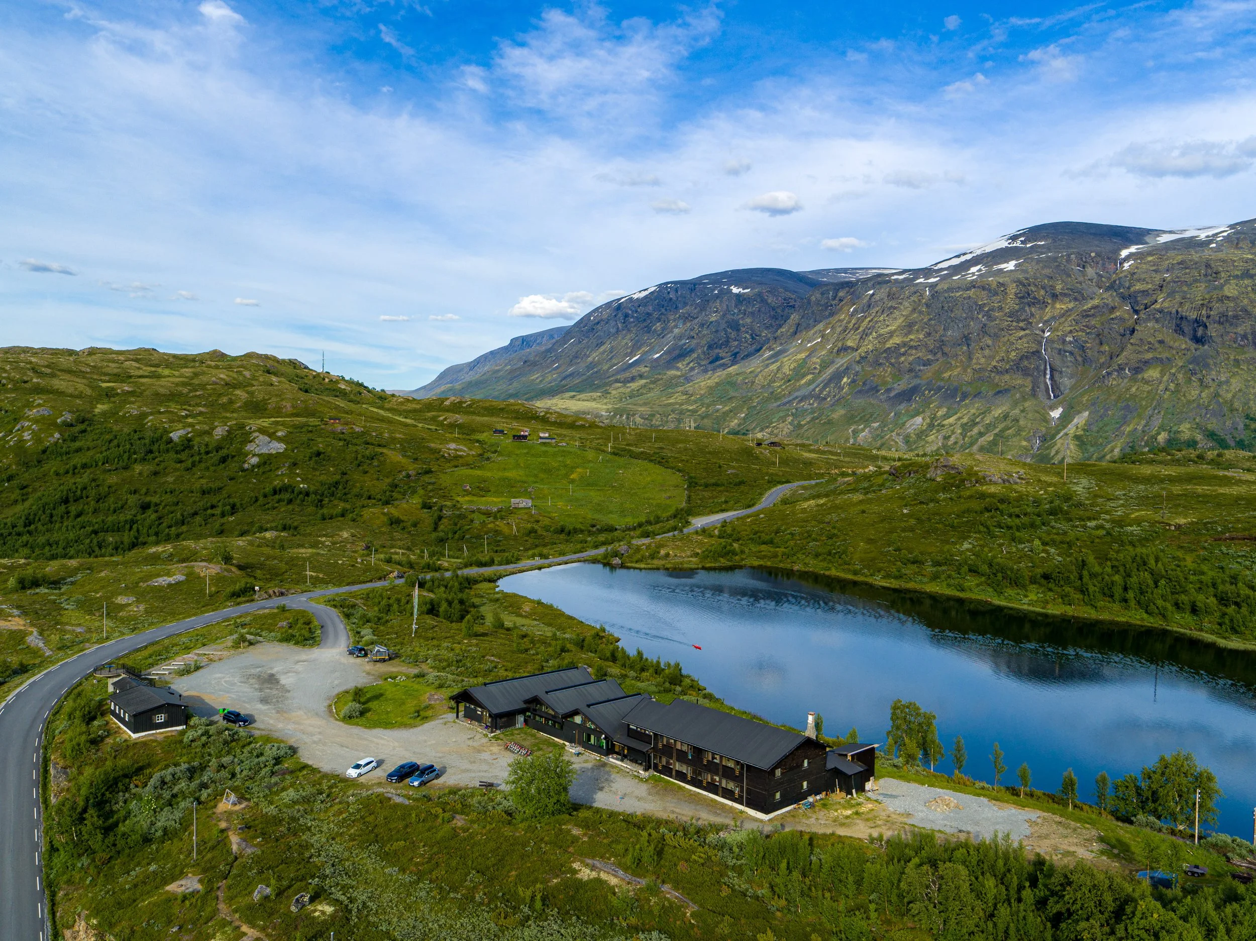 Vakker utsikt over fjell, innsjøer, og Jotunheimen Fjellstue, med grønne fjell og blå himmel.
