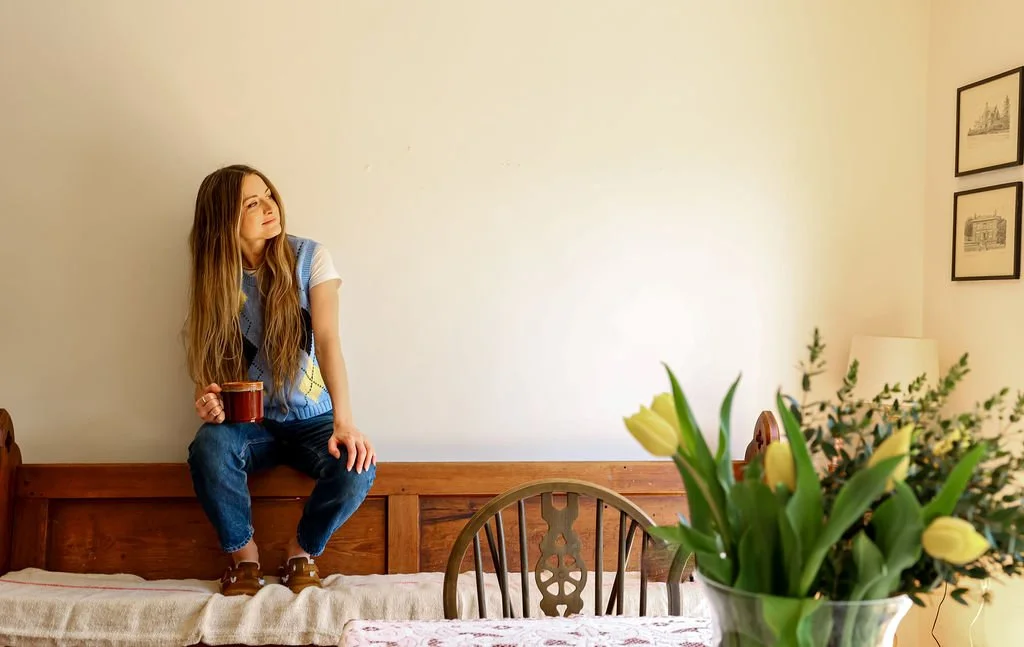 becca with cup of tea looking in distance with flowers in forground