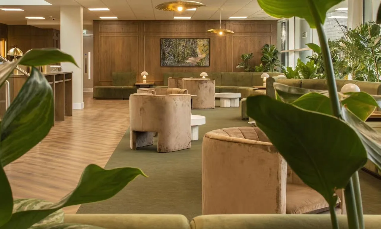 Modern lounge area with green and beige furniture, plants, and soft lighting.