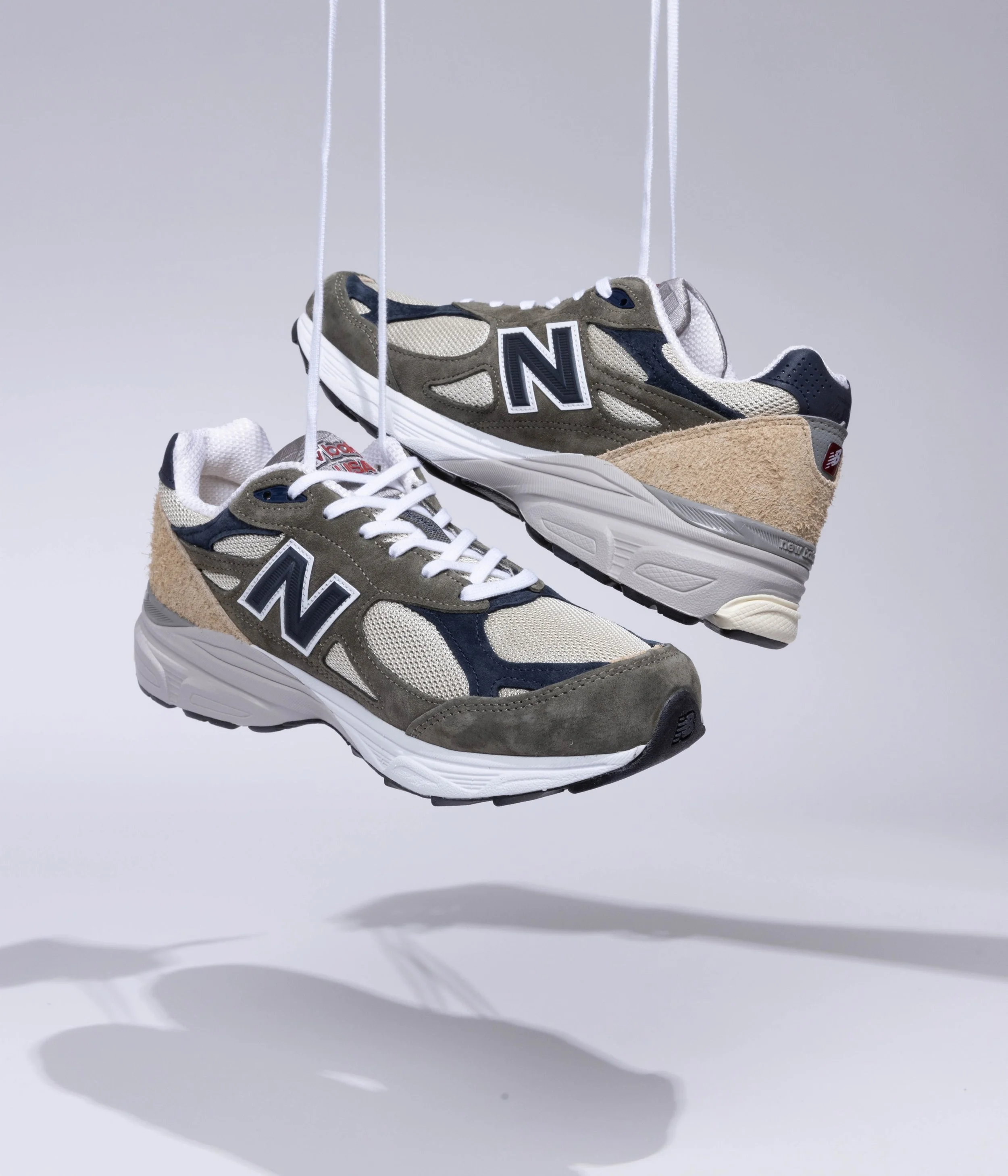 Une paire de baskets New Balance suspendues dans l'air, avec un fond blanc et une ombre en dessous.