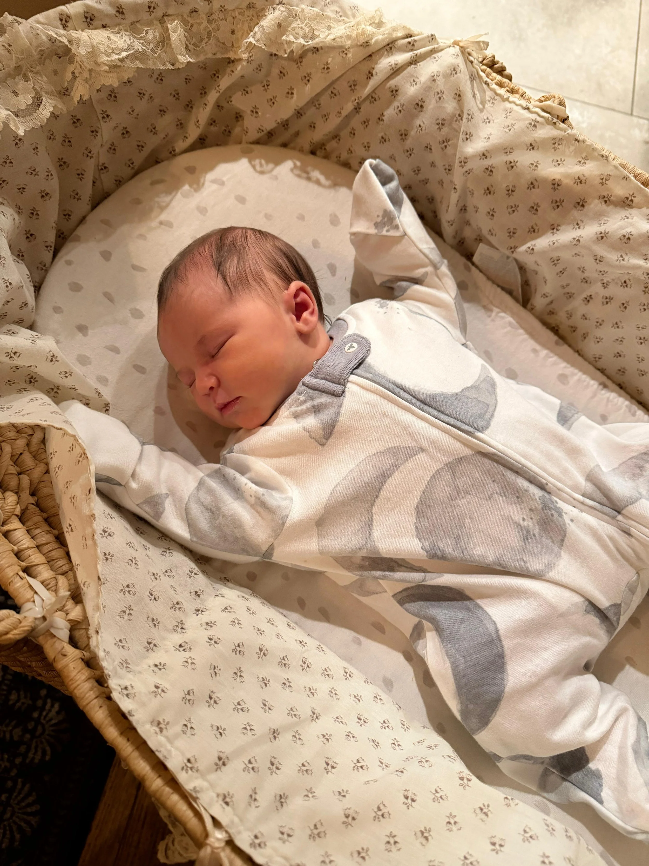 A newborn baby asleep with their arms up in a moses basket