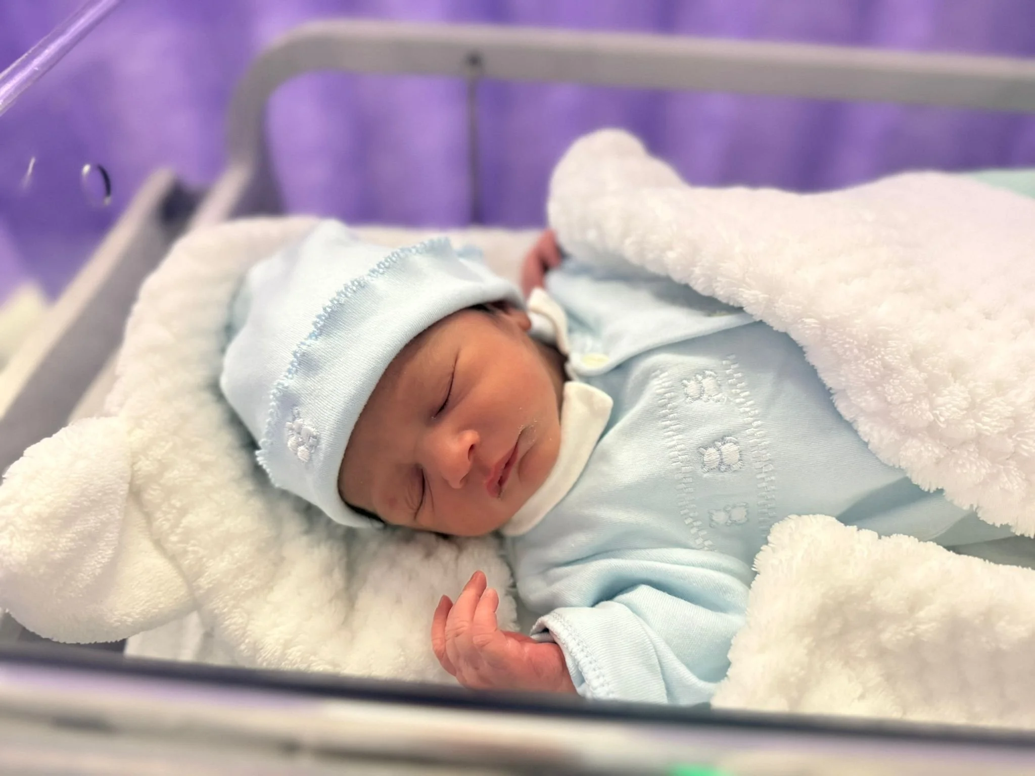 A newborn baby asleep in a hospital cot.