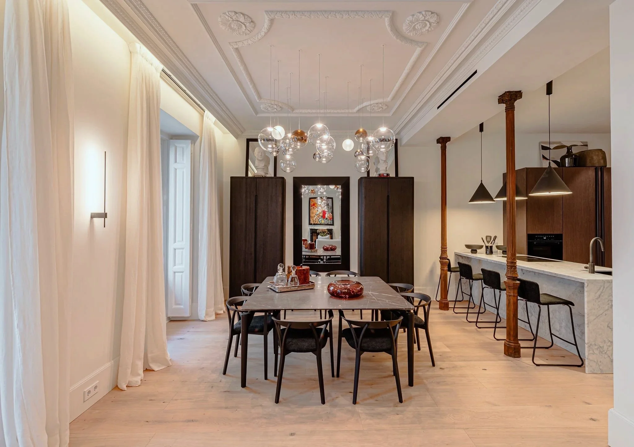 Interior de una sala de comedor moderna con mesa de mármol, sillas negras, cortinas blancas, lámparascolgantes de vidrio y techo decorado.