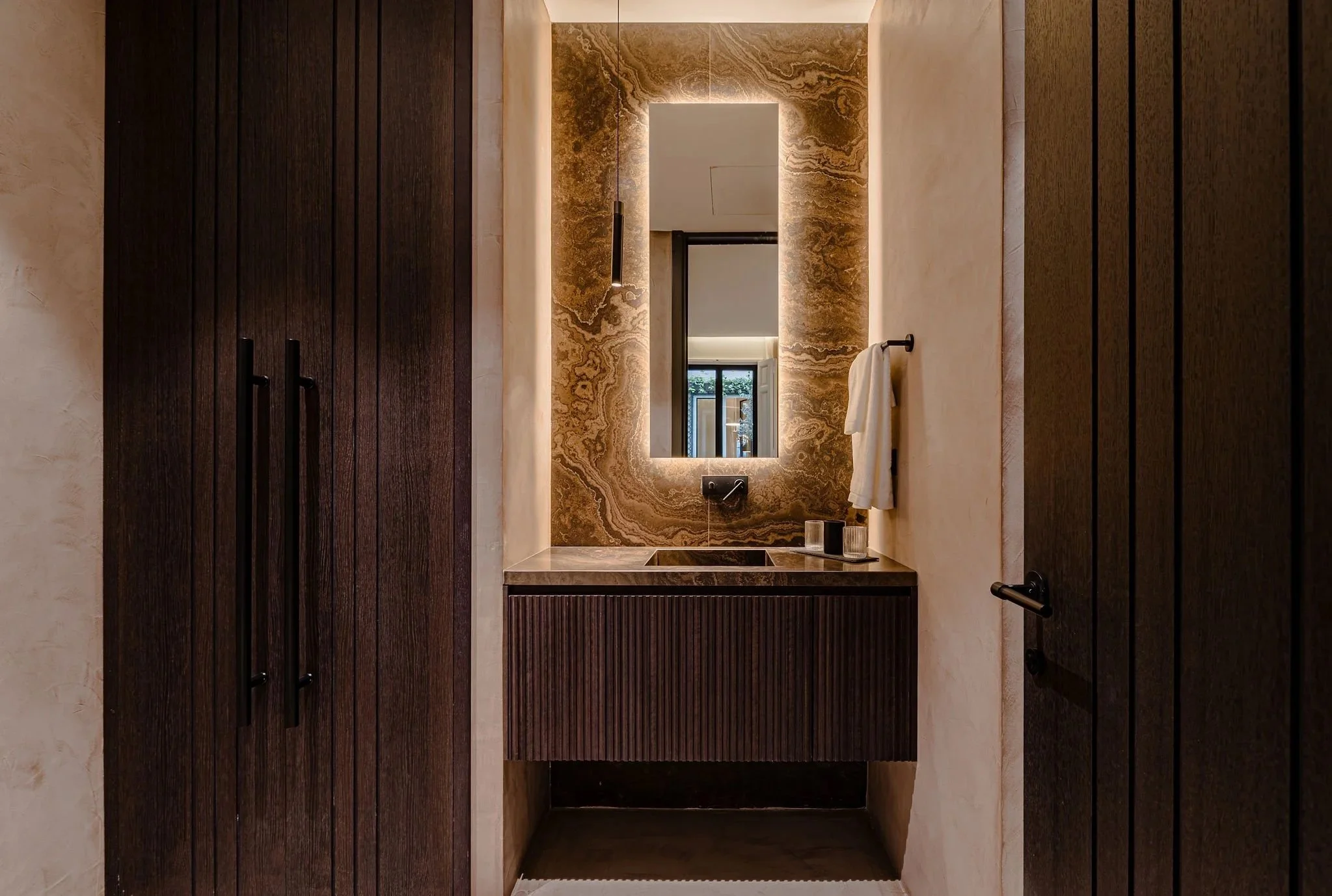Espejo con iluminación en un baño moderno, con paredes de mármol y madera.