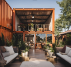 Outdoor lounge area with seating, plants, and a two-story container-style structure with a balcony, under a clear sky.