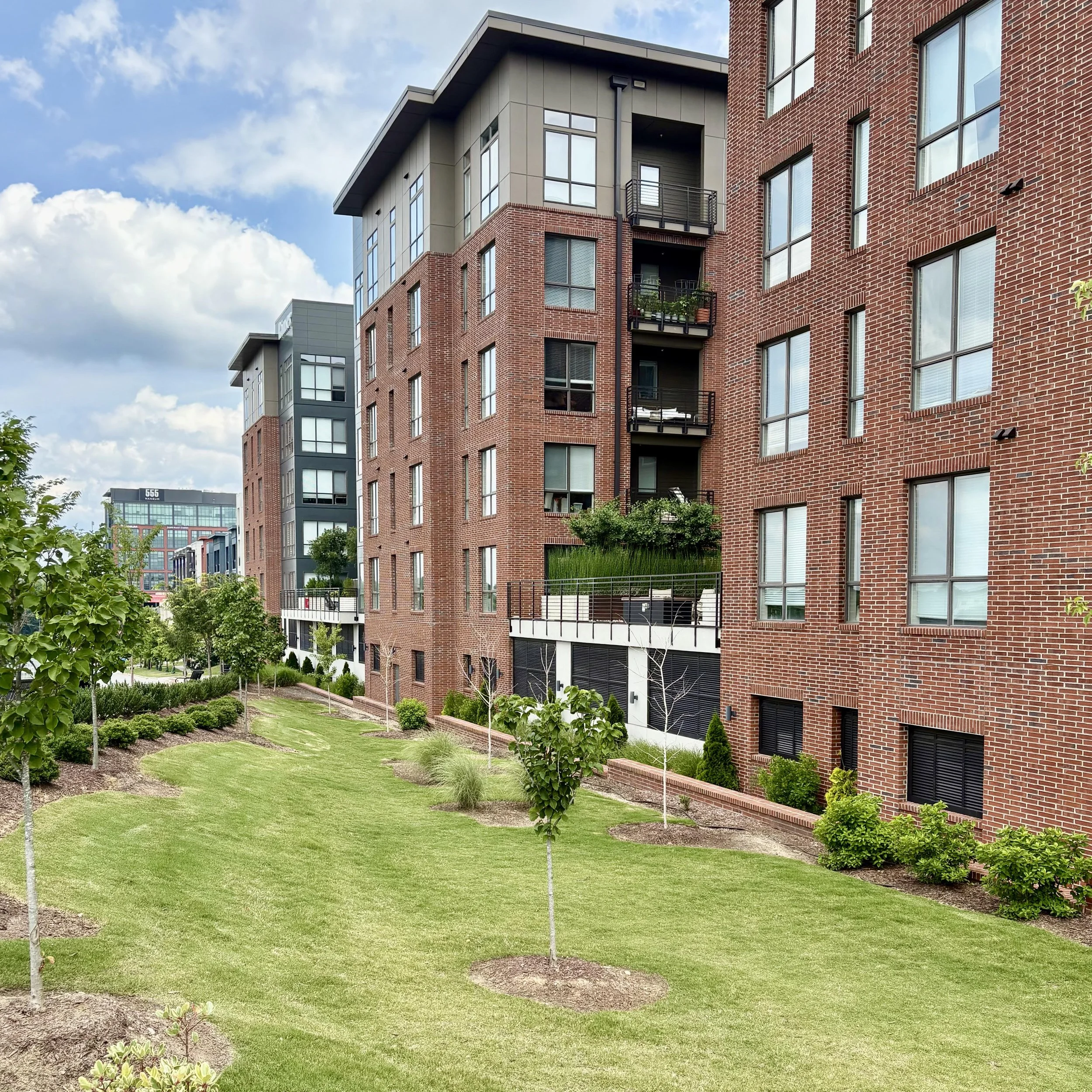 Modern building with wooden and white exterior, large glass window, surrounded by yellow flowers, mountains in the background, cloudy sky.
