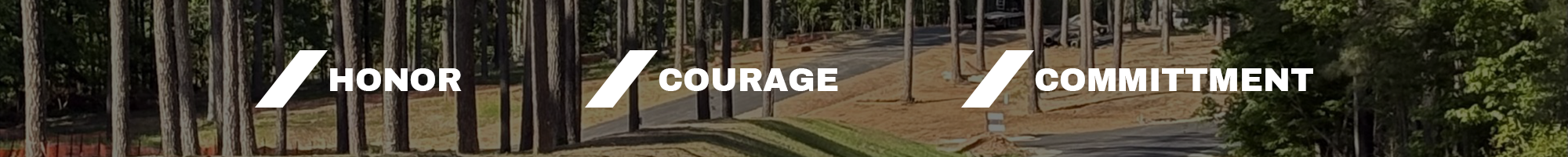 A natural outdoor scene with a road framed by trees and a promotional banner with the words 'Honor, Courage, Commitment' written across it.