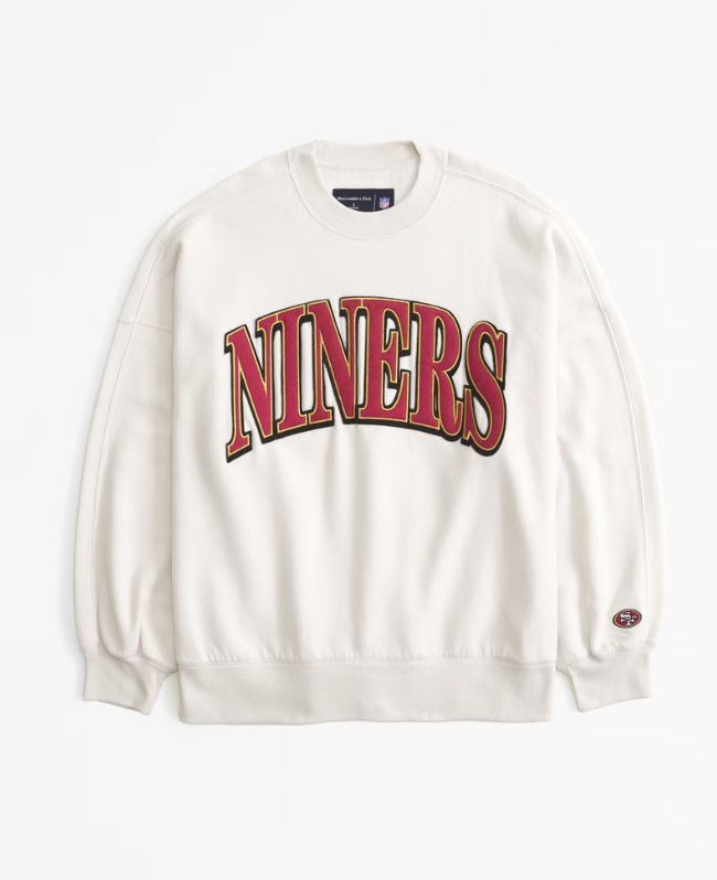 White sweatshirt with "NINERS" in red and gold lettering, small logo on sleeve.
