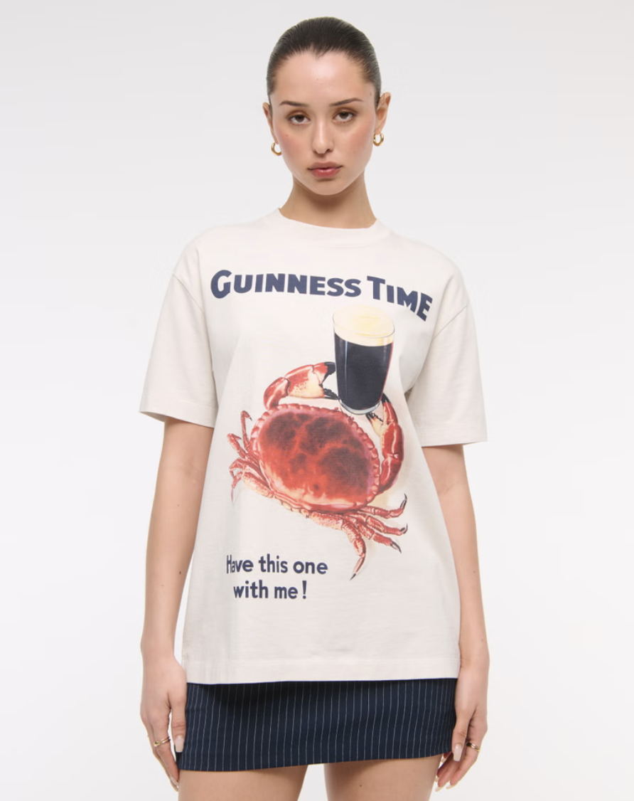 Person wearing a white "Guinness Time" t-shirt with a crab and a pint of Guinness graphic design.
