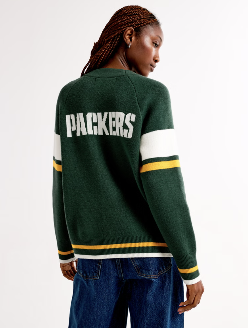 Person wearing a green sweater with 'PACKERS' on the back and white and yellow stripes on sleeves, paired with jeans.