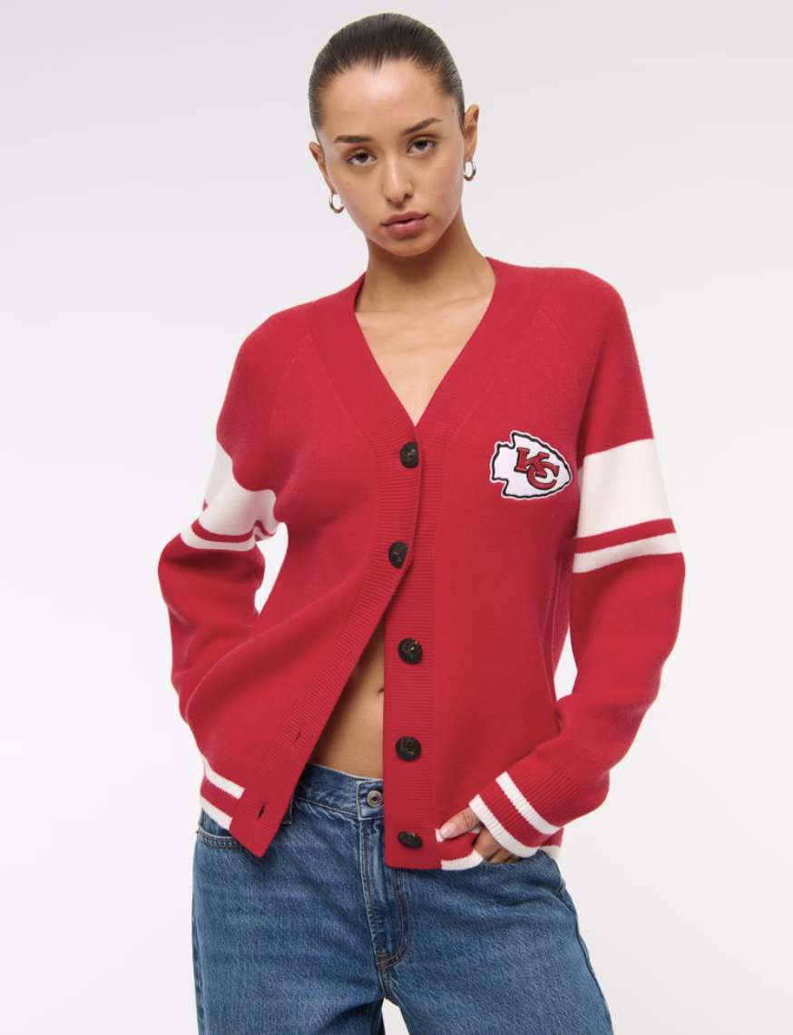 Person wearing a red cardigan with a Kansas City Chiefs logo, paired with blue jeans.