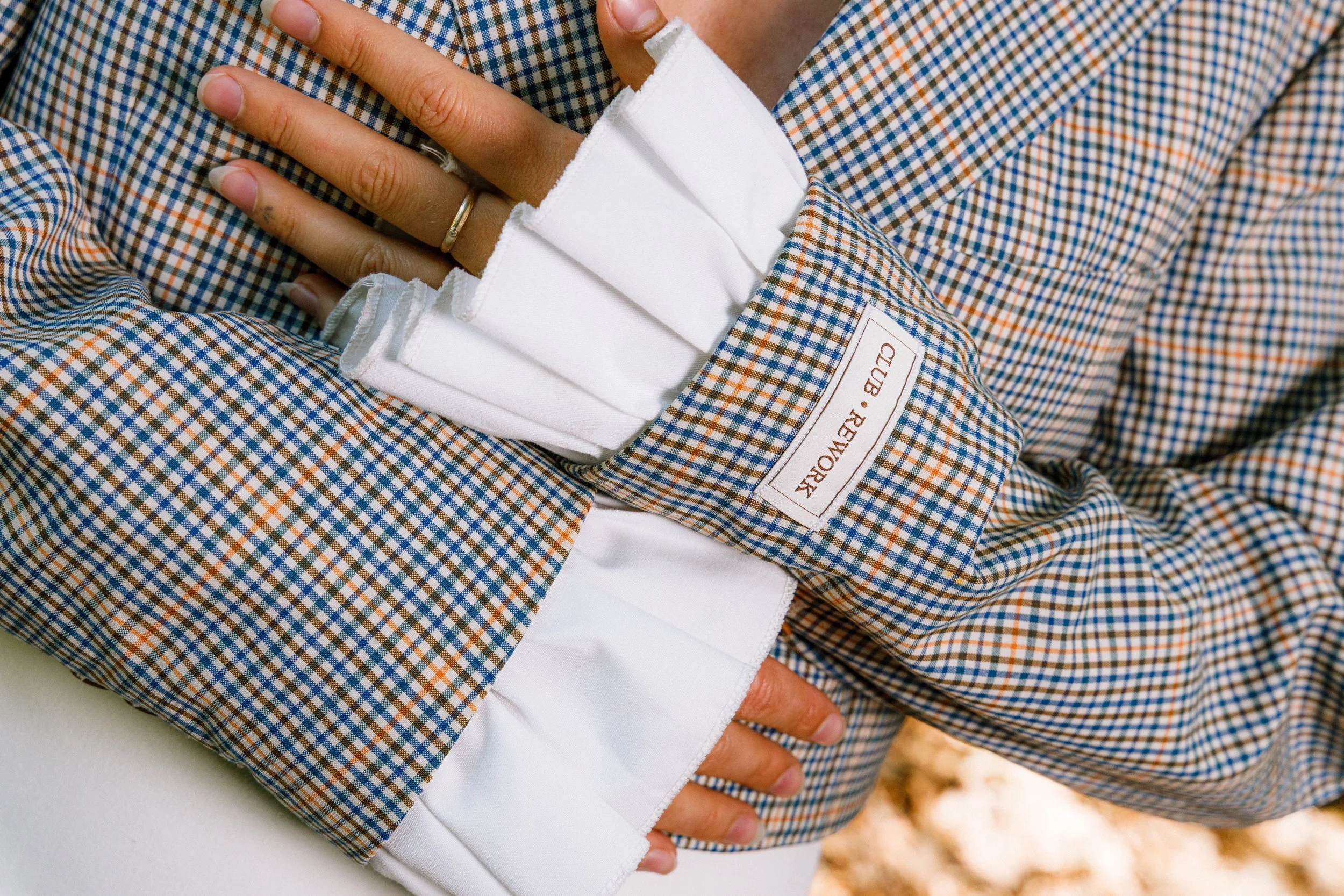 Persoon draagt een geruite blazer en witte handschoenen met een label 'Club Réwork'.