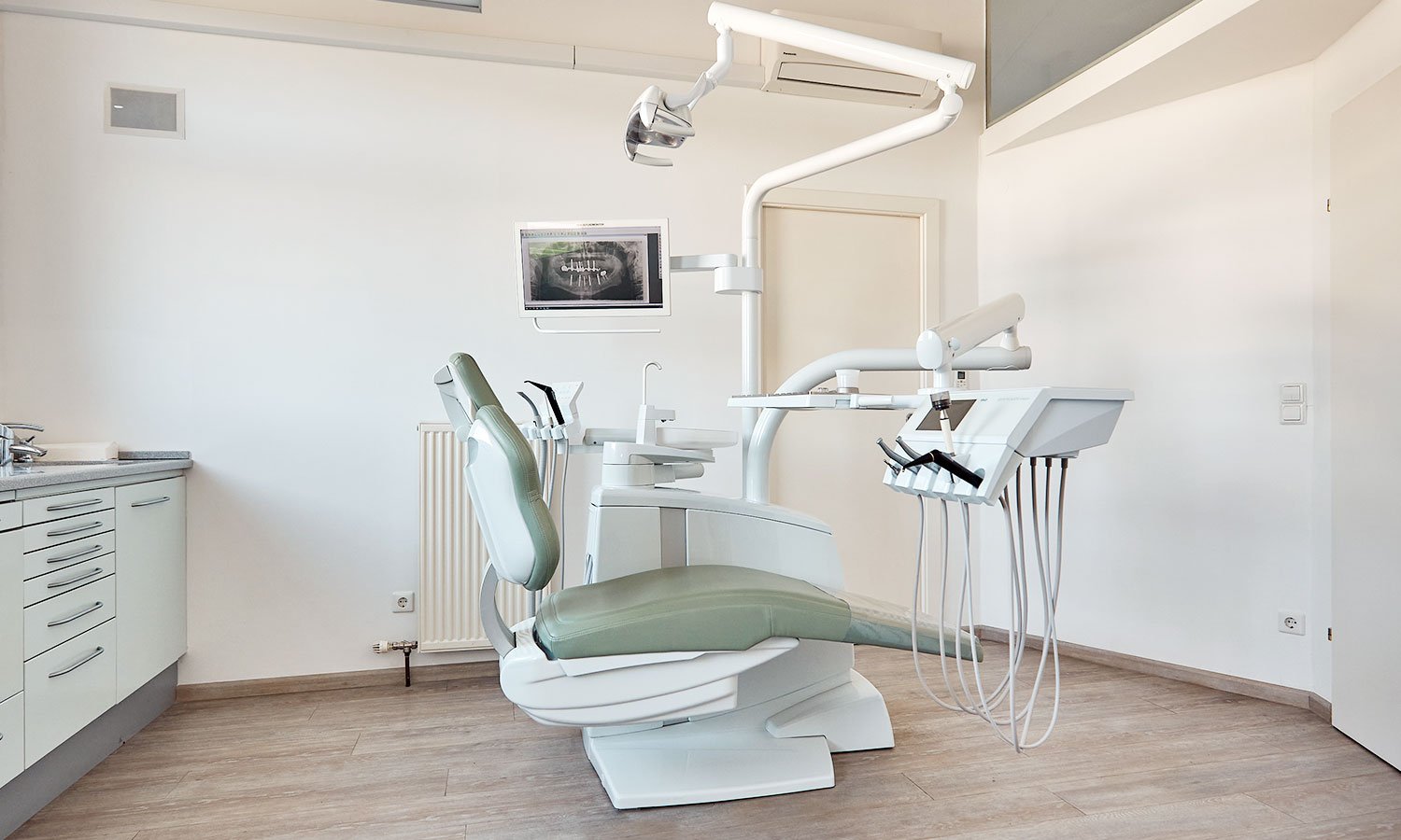 Modernes zahnmedizinisches Behandlungszimmer mit Dentaltisch, Stuhl, zahnärztlichen Geräten und Monitor.
