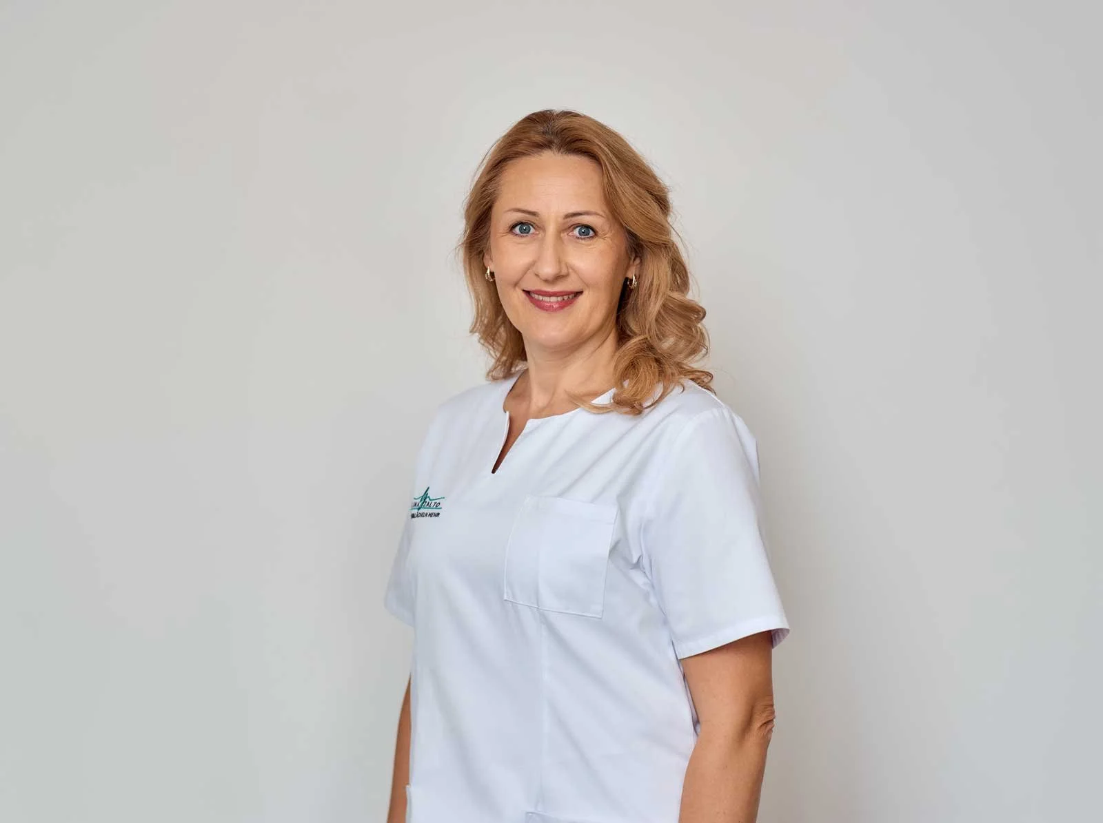 Porträt einer freundlichen Ärztin oder Krankenschwester mit roten, lockigen Haaren, in weißem Uniform, lächelnd, vor einem hellen Hintergrund.