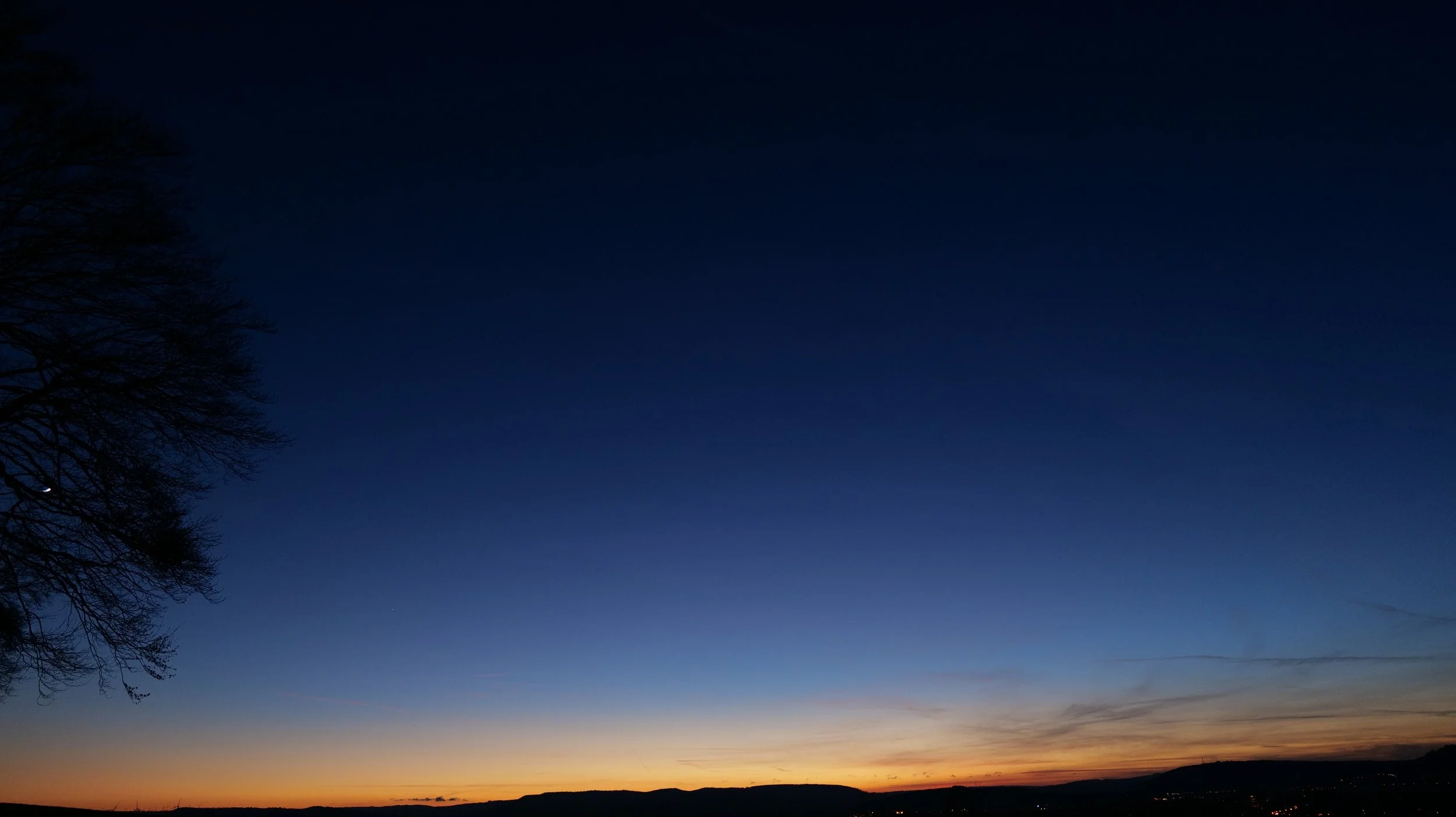 A sunset or sunrise sky with a gradient from deep blue to orange near the horizon, with silhouetted trees and landscape in the foreground.