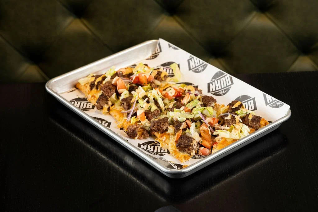 Pizza topped with ground beef, lettuce, diced tomatoes, and possibly other vegetables, served on a branded tray.