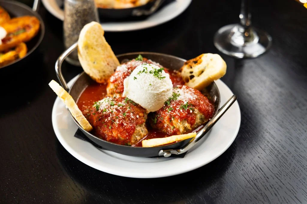 Meatballs with tomato sauce, served with grated cheese, bread slices, and a scoop of sour cream or ricotta cheese, garnished with chopped herbs.