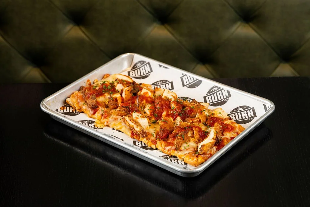 Pizza slice topped with meats and herbs on a branded tray.