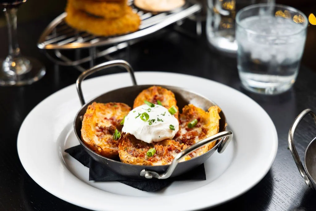 Baked stuffed potato halves topped with sour cream and chopped green onions, served in small metal skillet on a white plate.
