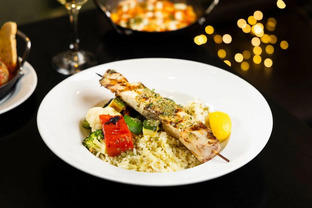 A plate of grilled fish skewer with rice and vegetables, served with lemon wedge