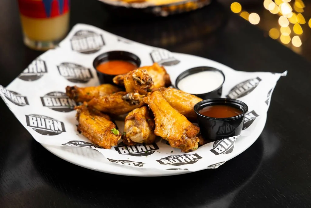 Fried chicken wings with three dipping sauces on a branded paper-lined plate.