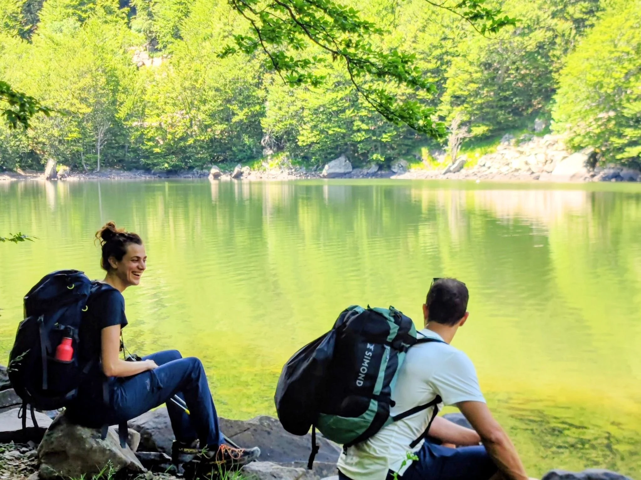 Due escursionisti davanti a un lago nel Parco dei 100 Laghi, nell’Appennino Parmense, con il bosco sullo sfondo