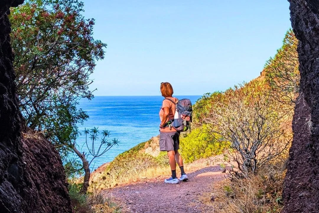 Escursionista sul Cammino di Santa Barbara che guarda il mare dall’interno di una grotta