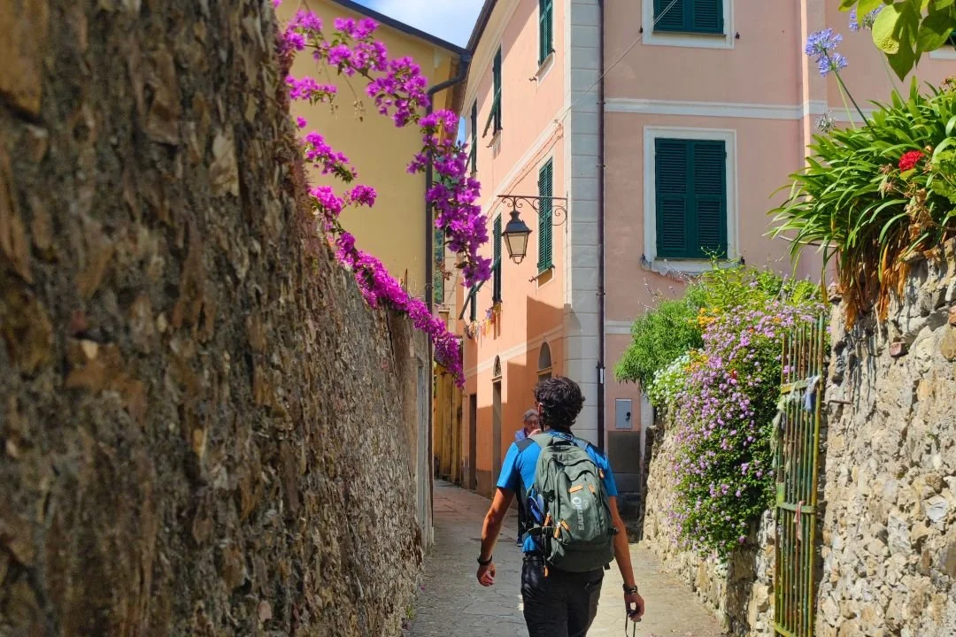 Escursionista in un vicolo di Frattura tra bougainvillea lungo il cammino in Liguria