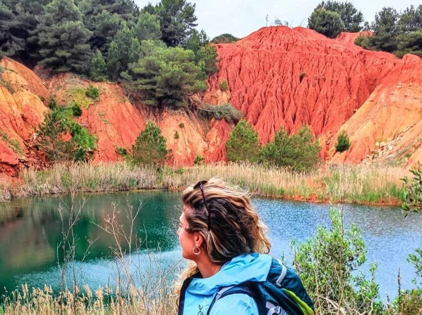 Ragazza escursionista davanti alla cava di bauxite di Otranto con il laghetto verde al centro, lungo il Cammino del Salento.