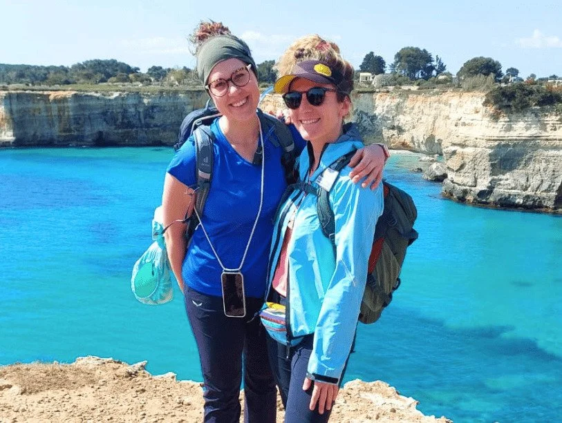 Due escursioniste abbracciate davanti ai faraglioni di Sant’Andrea lungo il Cammino del Salento.