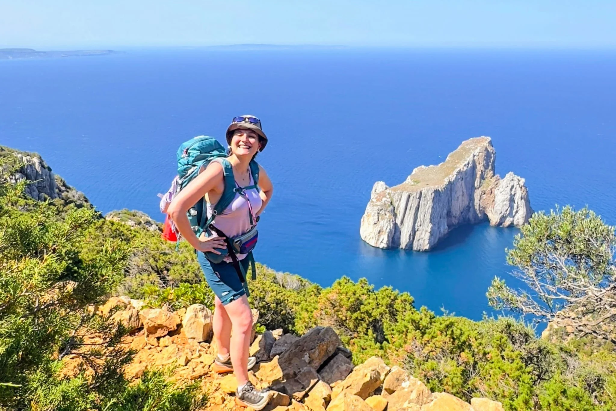 Ragazza con zaino che sorride davanti al mare della Sardegna sul Cammino Minerario di Santa Barbara