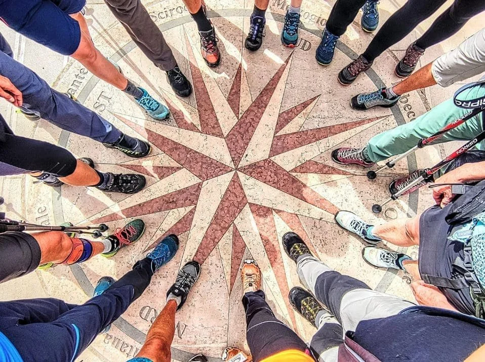 Scarpe di escursionisti disposte in cerchio sopra una rosa dei venti lungo il Cammino del Salento.