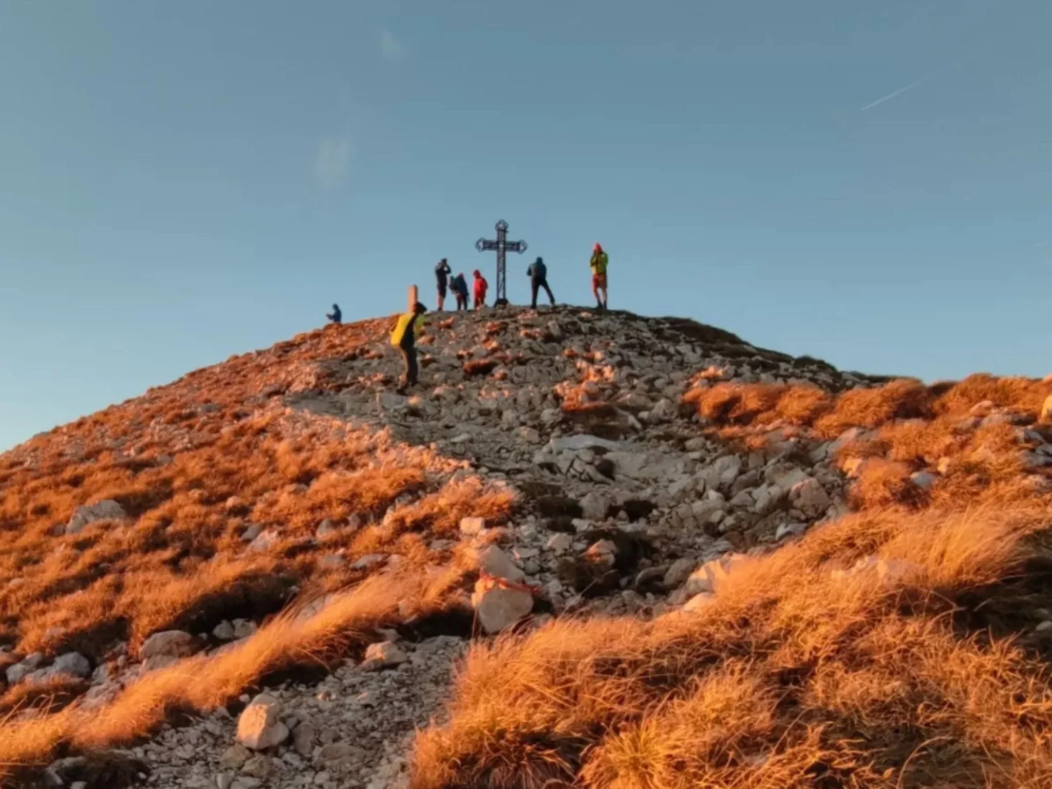 Escursionisti al tramonto sotto la croce di vetta del Monte Baldo