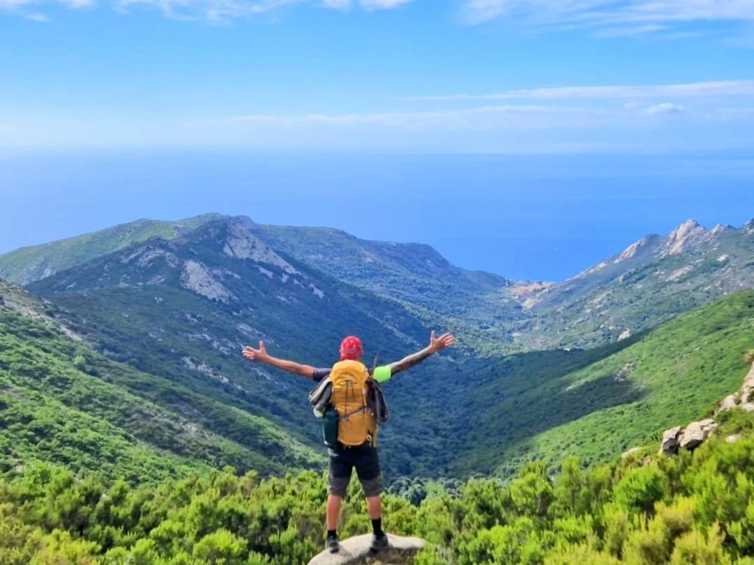 Escursionista sul sentiero con vista su una piccola cima immersa nella macchia mediterranea lungo la Grande Traversata Elbana