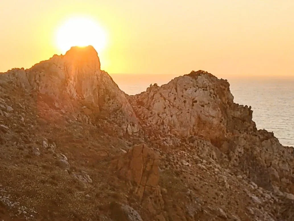 Tramonto sul Cammino Minerario di Santa Barbara in Sardegna con cielo arancione e vista panoramica sul mare